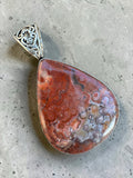 Making Waves Jewelry and Accessories teardrop Crazy Lace Agate pendant with silver filigree bail on concrete surface