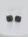 Making Waves Jewelry and Accessories square black druzy stud earrings with polished silver frames on a grey surface.