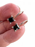 Making Waves Jewelry and Accessories sterling silver drop earrings with square-cut black stones held in fingers.