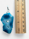 Making Waves Jewelry and Accessories blue agate geode slice pendant in a sterling silver setting next to a ruler.