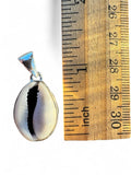 Making Waves Jewelry and Accessories cowrie shell pendant with silver setting next to a wooden ruler for scale