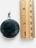 Making Waves Jewelry and Accessories round labradorite pendant in a sterling silver bezel next to a wooden ruler.