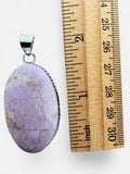 Making Waves Jewelry and Accessories oval lavender gemstone pendant in a sterling silver beaded bezel next to a ruler.