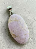 Making Waves Jewelry and Accessories lavender gemstone pendant in a sterling silver beaded bezel on a grey surface.