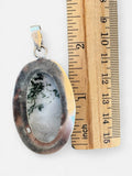 Making Waves Jewelry and Accessories oval moss agate pendant in 925 sterling silver next to a wooden ruler for scale