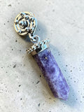 Making Waves Jewelry and Accessories purple crystal point pendant with silver spiral setting on a textured surface.