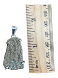 Making Waves Jewelry and Accessories raw pyrite stone pendant in a sterling silver setting next to a wooden ruler.