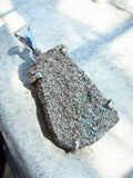 Making Waves Jewelry and Accessories raw pyrite pendant in a polished 925 sterling silver setting on a stone surface.