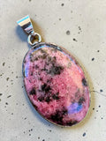 Making Waves Jewelry and Accessories oval rhodonite pendant with black inclusions in a polished sterling silver bezel.