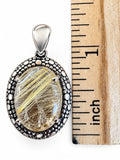 Making Waves Jewelry and Accessories oval rutilated quartz pendant in a beaded sterling silver setting next to a ruler.