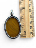 Making Waves Jewelry and Accessories oval Tiger's Eye pendant in 925 sterling silver next to a wooden ruler