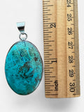 Making Waves Jewelry and Accessories oval turquoise pendant in a sterling silver bezel next to a wooden ruler.